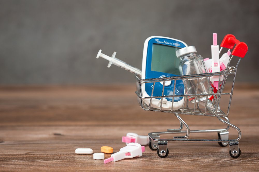 A table with miniature shopping cart. Inside the cart, there is a glucometer, an insulin syringe, and a few vials