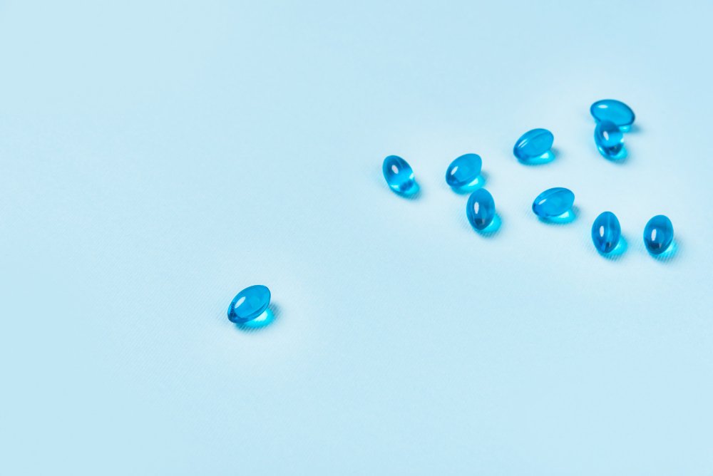Transparent blue color softgel capsules spread over a light blue surface