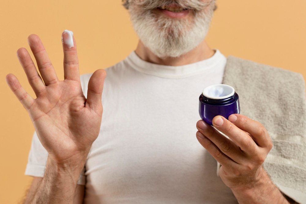 A man holding a cream bottle in the right hand, and has their right index finger dipped