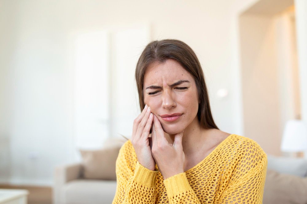 A woman in pain due to tooth ache. She is wearing a yellow sweater